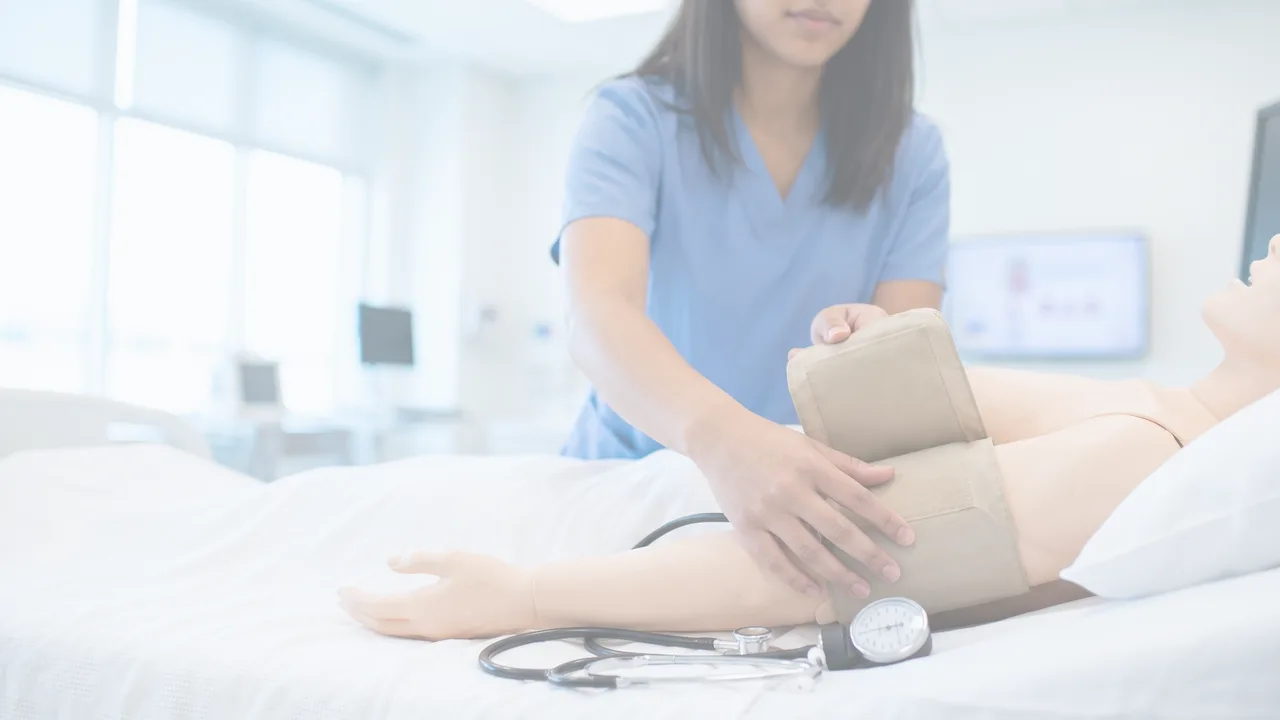 En salle de simulation, une soignante en uniforme installe un brassard de tension sur un mannequin.